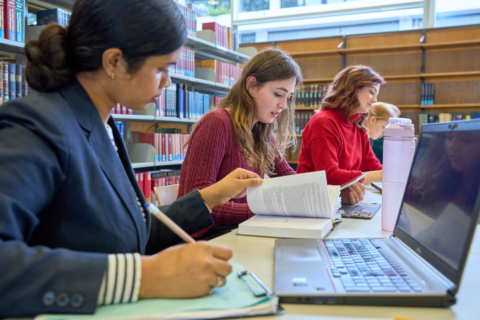 Eine Wissenschaftlerin und ein Wissenschaftler arbeiten hinter einer Glasfassade und mischen Chemikalien mit Großgeräten.
