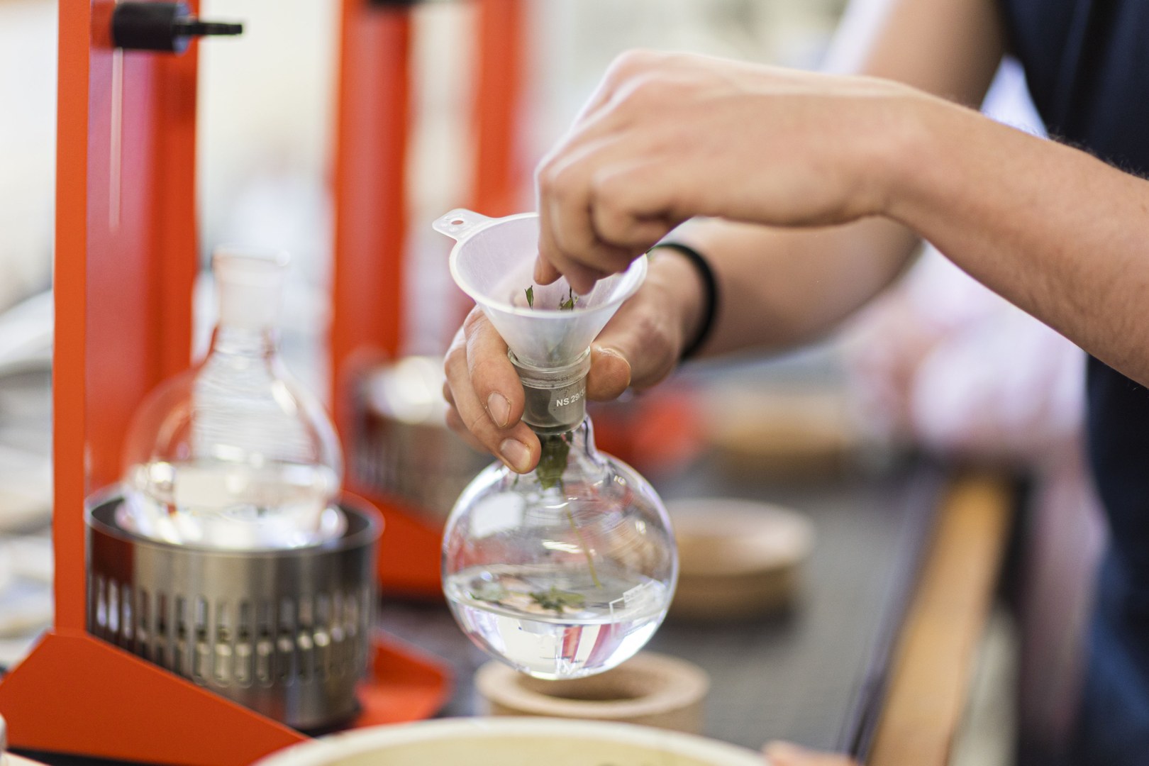 Eine Wissenschaftlerin und ein Wissenschaftler arbeiten hinter einer Glasfassade und mischen Chemikalien mit Großgeräten.